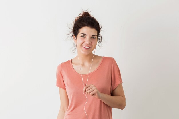 Retrato de uma jovem mulher bonita sorridente feliz hipster de aparência natural em uma camisa rosa posando isolado no fundo branco do estúdio, ouvindo música em fones de ouvido