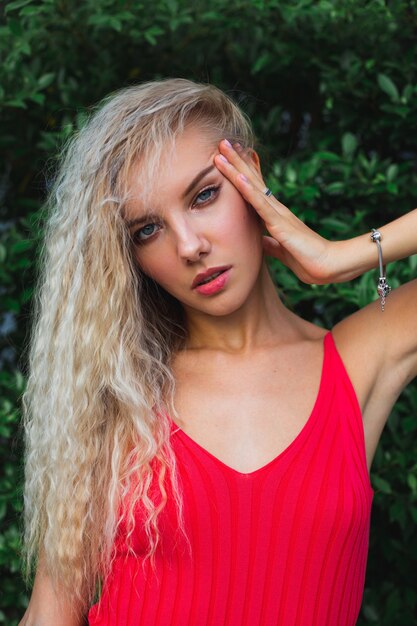 Retrato de uma jovem mulher branca em um vestido elegante de encaixe vermelho ao ar livre em um fundo de folhas tropicais.