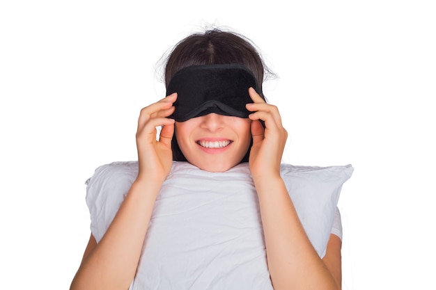 Retrato de uma jovem mulher cansada, usando máscara de dormir e segurando uma almofada no estúdio.