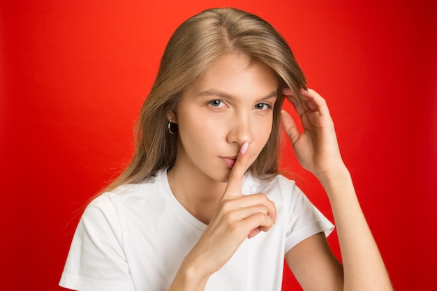 Retrato de uma jovem mulher caucasiana com emoções brilhantes na parede vermelha brilhante