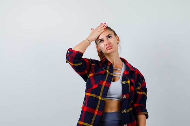 Foto grátis retrato de uma jovem mulher com a mão na testa em cima, camisa quadriculada e vista frontal pensativa