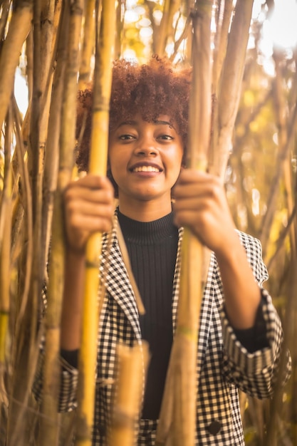Retrato de uma jovem mulher com cabelo afro em uma roupa formal atrás de plantas de bambu na Espanha