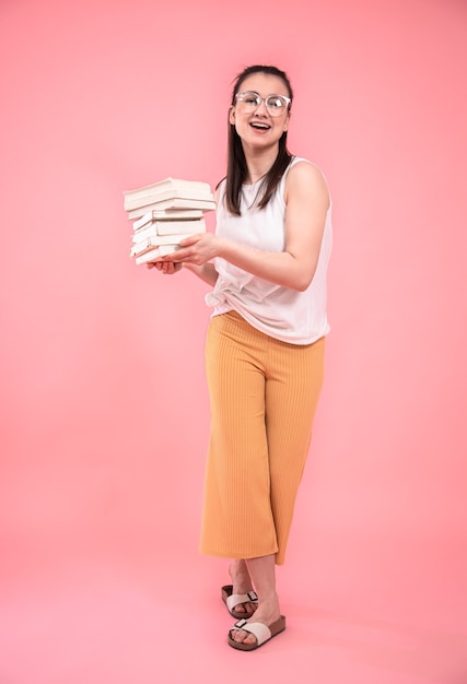 Retrato de uma jovem mulher com óculos em um comprimento total de fundo rosa. conceito de educação e hobbies.