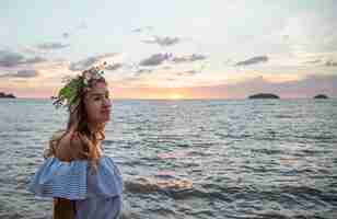 Foto grátis retrato de uma jovem mulher com uma composição de flores na cabeça no contexto do oceano ao pôr do sol.