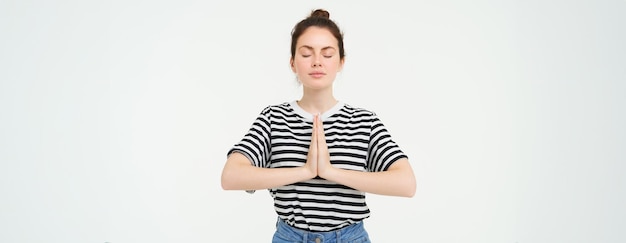 Foto grátis retrato de uma jovem mulher consciente meditando, segurando as mãos juntas, praticando o gesto namaste