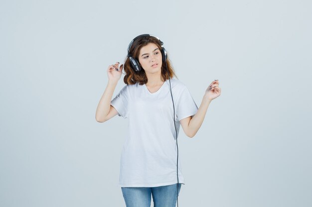 Retrato de uma jovem mulher curtindo música com fones de ouvido em uma camiseta branca, jeans e uma vista frontal de um sonho