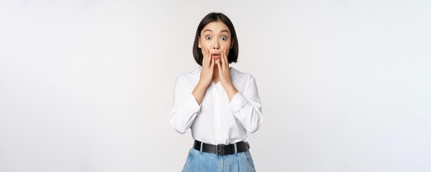 Retrato de uma jovem mulher de escritório surpreendida empresária asiática ofegando espantada dizendo uau, impressionada com as notícias contra o fundo branco