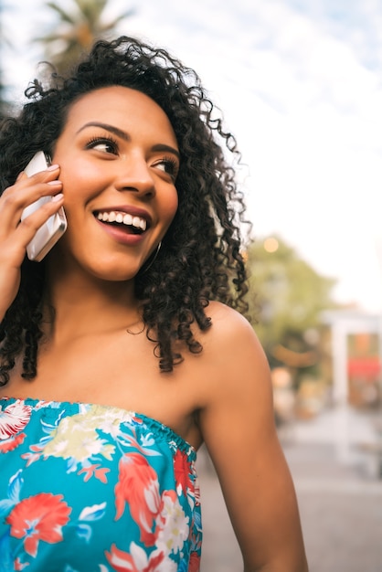 Retrato de uma jovem mulher latino-americana afro falando ao telefone, ao ar livre na rua. Conceito de tecnologia.