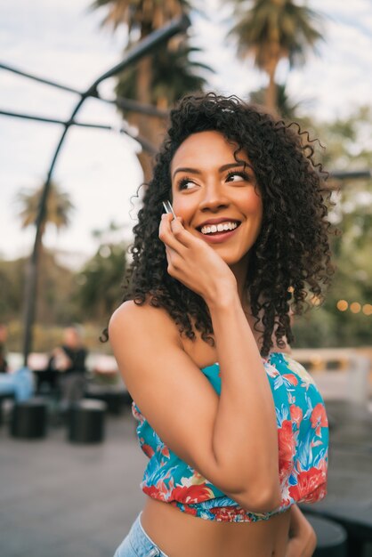 Retrato de uma jovem mulher latino-americana afro falando ao telefone, ao ar livre na rua. Conceito de tecnologia.