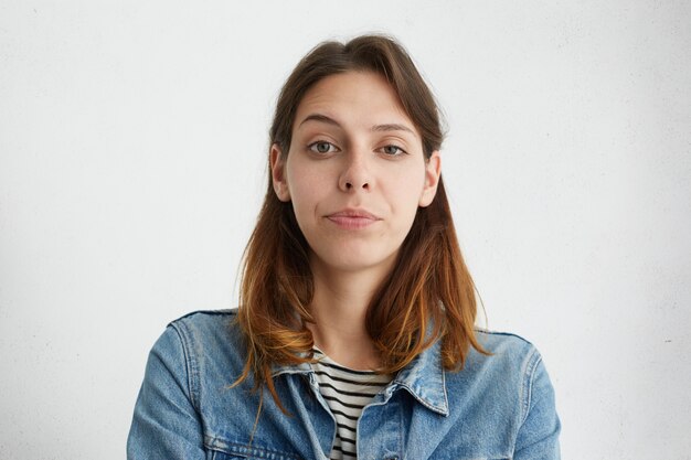 retrato de uma jovem mulher levantando a sobrancelha com admiração, vestida com jaqueta jeans isolada. Mulher suspeita franzindo a testa.