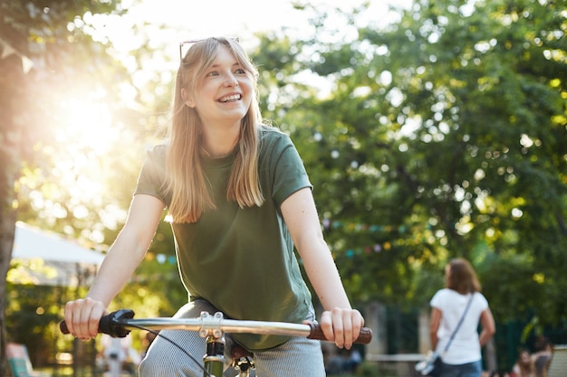 Retrato de uma jovem mulher loira bonita fingindo andar de bicicleta no parque durante um festival de comida