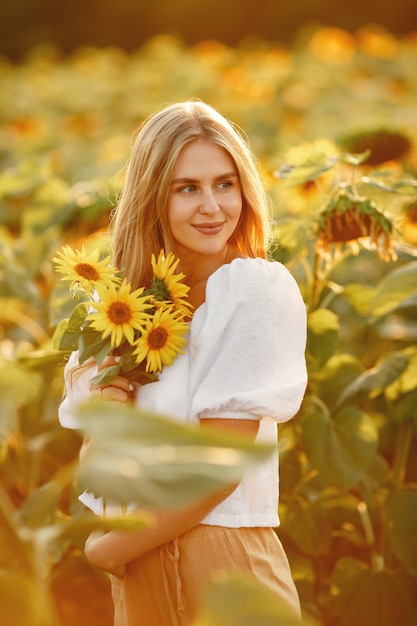 Retrato de uma jovem mulher loira bonita no campo de girassóis na luz de fundo. Conceito de campo de verão. Mulher e girassóis. Luz de verão. Beleza ao ar livre.