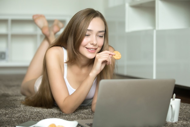 Retrato de uma jovem mulher, mentindo, observando o laptop