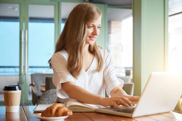 Retrato de uma jovem mulher relaxada, digitando no laptop sentado na mesa do café
