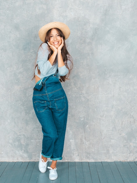 Retrato de uma jovem mulher sorridente bonita olhando. Menina na moda em roupas de verão casual macacão e chapéu.