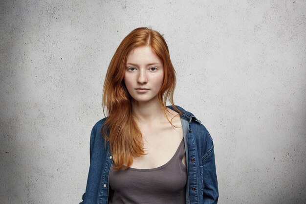 Retrato de uma jovem ruiva caucasiana com sardas vestida com camisa jeans por cima posar isolado olhando sério ou chateado.