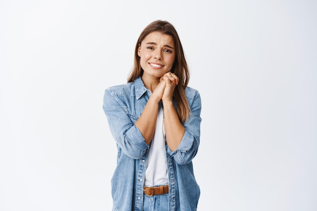 Retrato de uma jovem se sentindo tocada e animada, segurando as mãos perto do rosto e derretendo por causa de algo lindo ou romântico, olhando fascinada, branca