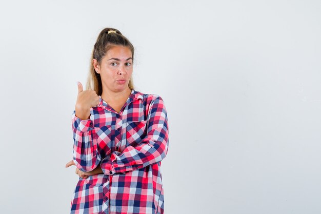 Retrato de uma jovem senhora aparecendo com o polegar em uma camisa xadrez