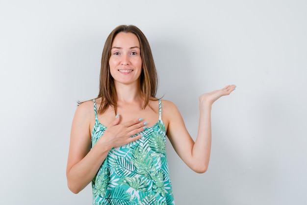 Retrato de uma jovem senhora com a mão no peito, segurando algo na blusa e olhando a vista frontal alegre