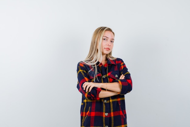 Retrato de uma jovem senhora em pé com os braços cruzados em uma camisa xadrez e com uma vista frontal confiante