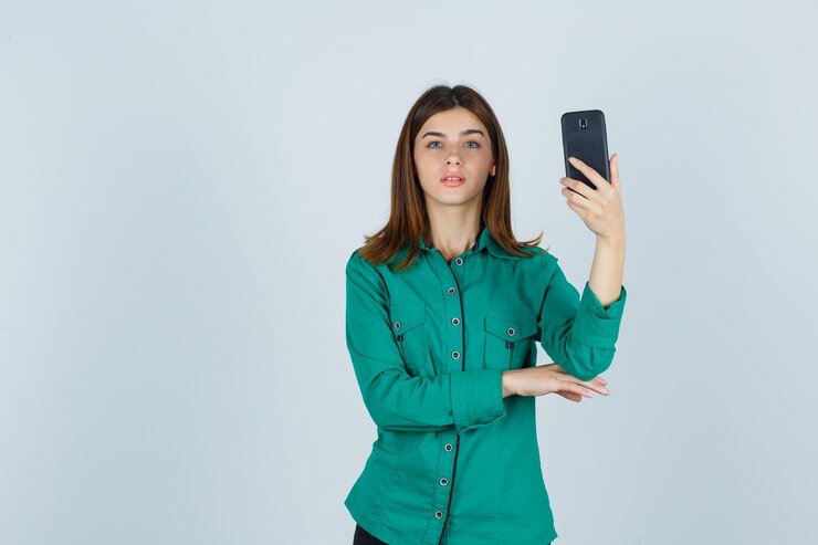 Foto grátis retrato de uma jovem senhora segurando um telefone celular com uma camisa verde e olhando séria para a frente