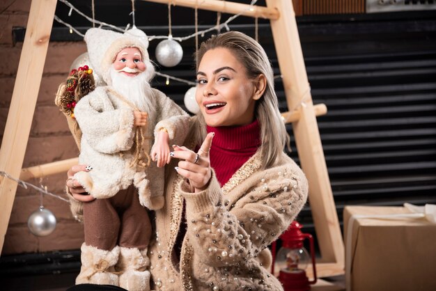 Retrato de uma jovem sentada no chão segurando um brinquedo de Papai Noel. Foto de alta qualidade.