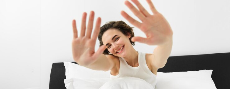 Foto grátis retrato de uma jovem sonolenta e feliz que acorda em sua cama estendendo as mãos escondendo o rosto de