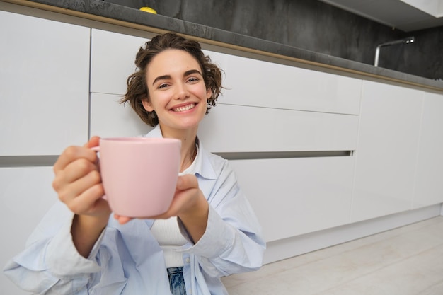 Retrato de uma jovem sorridente satisfeita recomendando sua bebida mostra uma xícara rosa de chá ou café com ha