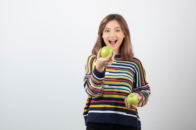 Retrato de uma jovem sorridente segurando duas maçãs verdes frescas.