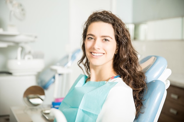 Retrato de uma jovem sorridente sentada na cadeira na clínica odontológica