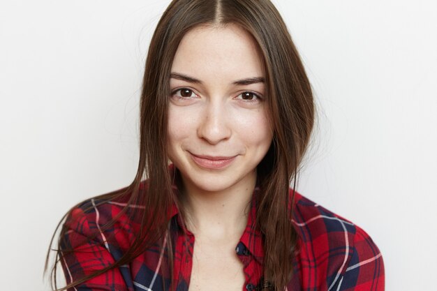 Retrato de uma linda adolescente com cabelo bagunçado e sorriso fofo, vestindo uma camisa xadrez vermelha