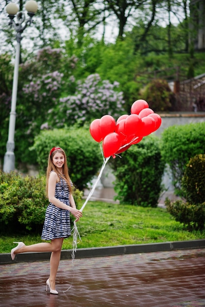 Retrato de uma linda e linda dama de honra em um lindo vestido segurando balões vermelhos em forma de coração no parque na festa de despedida de solteira