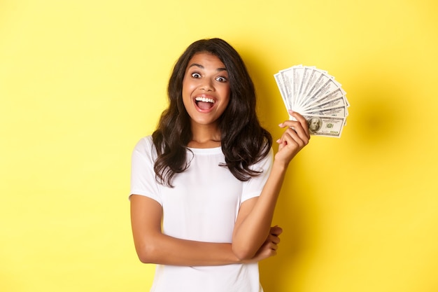 Retrato de uma linda garota afro-americana sorrindo feliz e mostrando dinheiro indo às compras em pé