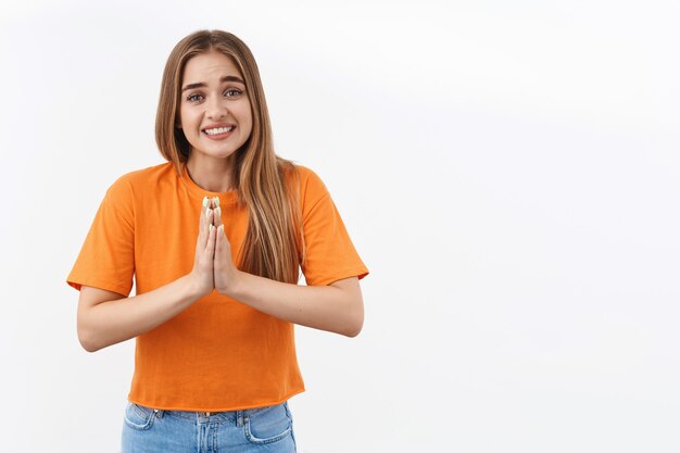 Retrato de uma linda garota boba precisa de ajuda o mais rápido possível, cerrar os dentes fazendo um sorriso suplicante, de mãos dadas rezando, diga por favor, implorando favor, emprestando dinheiro de um amigo, pedindo algo