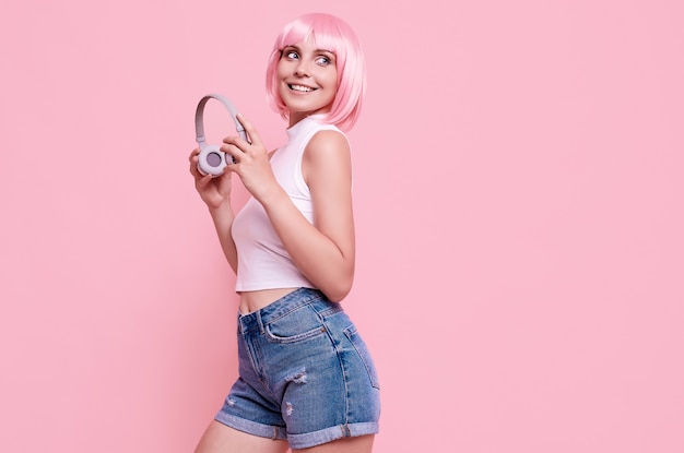Retrato de uma linda garota hippie brilhante com cabelo rosa curtindo a música em fones de ouvido coloridos