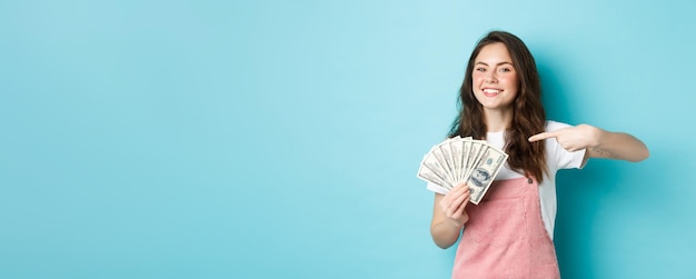 Retrato de uma linda garota sorrindo orgulhoso e satisfeito apontando o dedo para o dinheiro dólar mostrando bil dólar