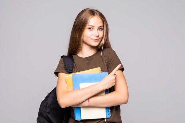 Retrato de uma linda jovem morena estudante segurando cadernos de exercícios isolados na parede branca