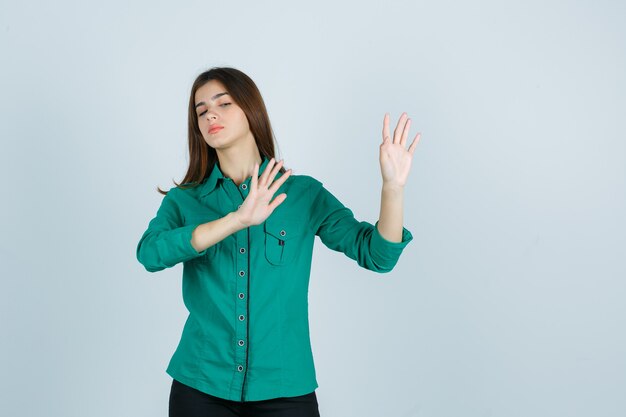 Retrato de uma linda jovem mostrando um gesto de parada com uma camisa verde e olhando de frente com irritação