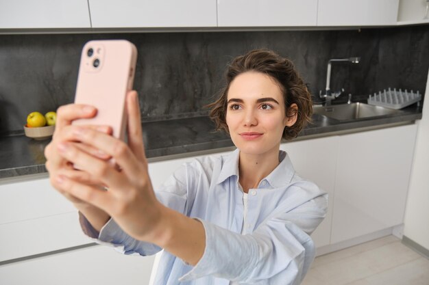 Retrato de uma linda jovem tirando selfie no celular em casa posa para foto com