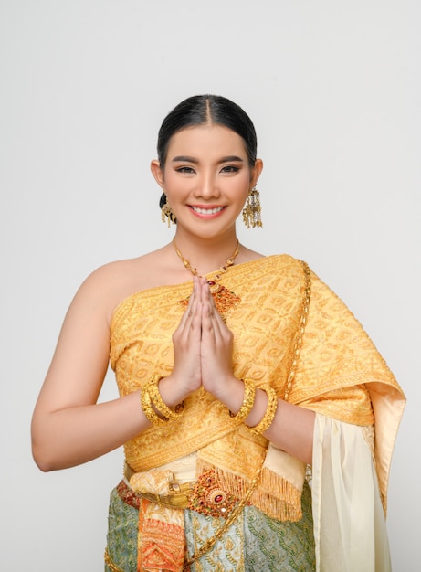 Retrato de uma linda mulher asiática em traje de vestido tradicional tailandês sorri e pose graciosamente na parede branca