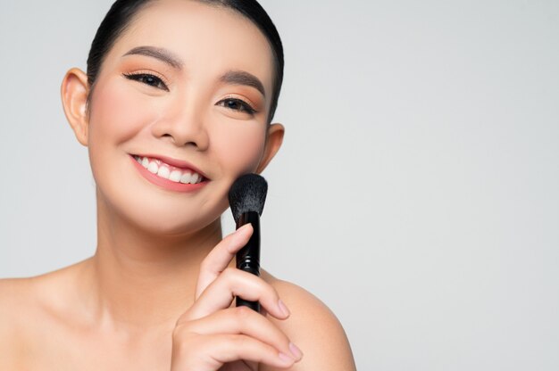 Retrato de uma linda mulher asiática segurando um pincel para blush de maquiagem