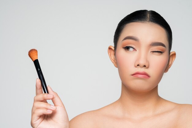 Retrato de uma linda mulher asiática segurando um pincel para blush de maquiagem