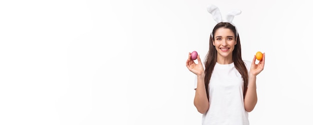Foto grátis retrato de uma linda mulher caucasiana em orelhas de coelho mostrando dois ovos coloridos e sorrindo parabenizando
