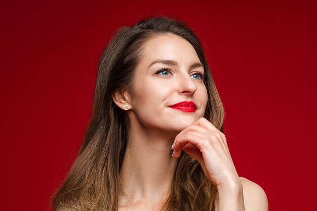 Retrato de uma linda mulher com cabelo castanho e lábios vermelhos, olhando para longe pensativamente e segurando a mão no queixo.