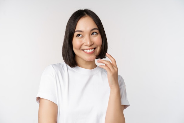 Retrato de uma linda mulher coquete rindo e sorrindo olhando de lado pensando pensativo ou imaginando algo em camiseta branca sobre fundo de estúdio