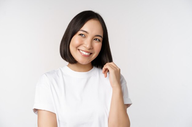 Retrato de uma linda mulher coquete rindo e sorrindo olhando de lado pensando pensativo ou imaginando algo em camiseta branca sobre fundo de estúdio