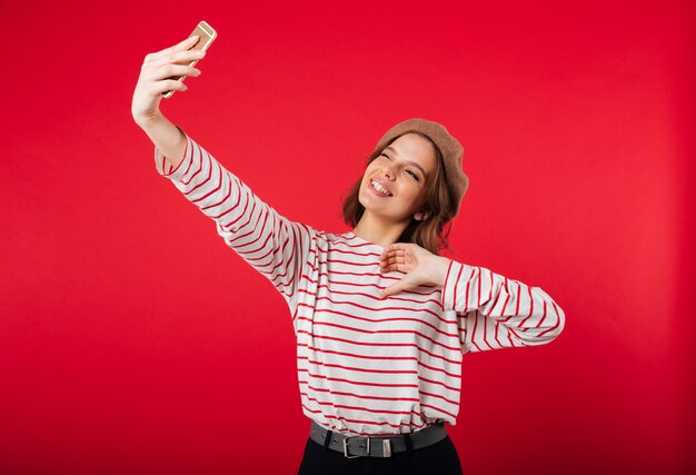 Retrato de uma linda mulher usando boina tomando uma selfie