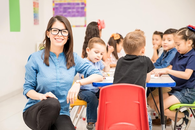 Retrato de uma linda professora de pré-escola hispânica amando seu trabalho e se divertindo com seus alunos