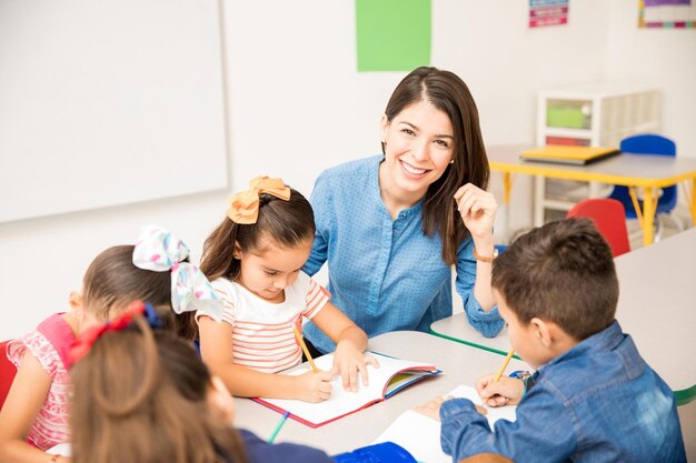 Retrato de uma linda professora de pré-escola hispânica ensinando seus alunos em uma sala de aula