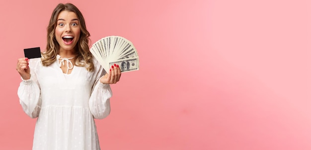 Retrato de uma loira bonita e feliz em vestido branco ganhando dinheiro com boa aposta feita d